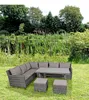 A wicker sectional sofa with cushions and a coffee table is set up on a grassy lawn next to a pond with reeds. Produktbild-Vorschau