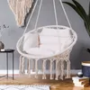 A macrame hanging chair with cushions is shown in a room with a gray wall and wooden floor. Podgląd zdjęcia produktu