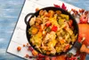 A close-up view of a cooked vegetable dish in a black pan, surrounded by autumn decorations like pumpkins and leaves. Náhled obrázku produktu