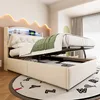 A beige upholstered bed with its storage compartment open, revealing stored items. The bed has a tufted headboard and a decorative wavy headboard with LED lighting. A green blanket is draped over the bed. Náhľad obrázku produktu