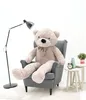 A large teddy bear sits in a gray armchair next to a floor lamp and a small side table with decorative items. Voir les images du produit