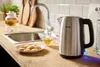 A kitchen counter with a kettle, tea cup, and cookies next to a sink. Náhľad obrázku produktu