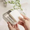 A person is holding a white bar of soap over a silver soap dish with a drainage rack. Produktbild-Vorschau