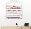 A white wall-mounted nail polish rack filled with various colors of nail polish bottles. Below the rack, on a wooden dresser, are a small white security camera and a digital clock displaying the time. Podgląd zdjęcia produktu