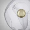 A close-up of a golden sphere within a translucent, swirling white material against a light gray background. Voir les images du produit