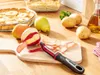 A kitchen scene with fruits, vegetables, and a peeler on a wooden countertop. Produktbild-Vorschau