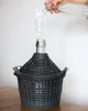 A hand is pouring liquid from a bottle into a carboy with an airlock attached. Produktbild-Vorschau