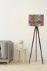 A floor lamp with a patterned lampshade stands next to a sofa and a small side table with a plant. Produktbild-Vorschau