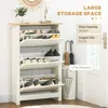 A white shoe cabinet with multiple flip-down drawers filled with shoes, placed in a room next to a door and an umbrella stand. The top surface has decorative items and a plant. Produktbild-Vorschau