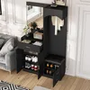A black entryway storage unit with a mirror, shoe cabinets, and a bench, placed next to a grey sofa and a white door. Podgląd zdjęcia produktu