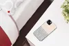 A phone case with a polka dot pattern is placed on a white nightstand next to a bed. Produktbild-Vorschau