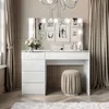 A white vanity table with a mirror and lights, decorated with framed pictures and a vase of flowers, in a room with beige curtains. Produktbild-Vorschau