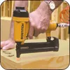 A person is using a yellow and black nail gun on a wooden surface. Podgląd zdjęcia produktu