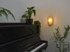 A wall lamp illuminates a corner with a piano and plants. Podgląd zdjęcia produktu