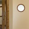 A round ceiling light fixture with a wooden frame is mounted on a light beige wall, next to a wooden door frame. Produktbild-Vorschau