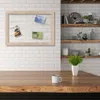 A wooden picture frame with photos is displayed on a white brick wall above a wooden table with a mug and a plant. Produktbild-Vorschau