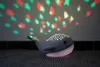 A whale-shaped night light projects stars onto a wall. Produktbild-Vorschau