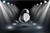 A white gaming headset is displayed under spotlights on a dark stage. Produktbild-Vorschau