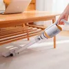 Weißer und oranger kabelloser Stabstaubsauger, der zum Reinigen unter einem Holztisch auf einem hellen Teppich verwendet wird Produktbild-Vorschau