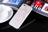 A white phone case with a floral pattern is placed on a black reflective surface, next to a white cup and saucer. A magazine is open in the background. Produktbild-Vorschau
