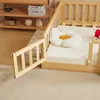 A wooden crib with a open gate and a flower-shaped pillow on the mattress. Produktbild-Vorschau