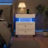 A white nightstand with LED lighting is placed next to a bed in a bedroom. Podgląd zdjęcia produktu