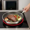A hand is holding a frying pan with a steak and vegetables cooking on an induction stove. Produktbild-Vorschau