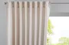 A close-up view of a beige curtain hanging from a curtain rod, with a blurred green outdoor scene visible through the window behind it.