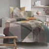 A neatly made bed with a geometric patterned duvet cover and pillows, set against a minimalist bedroom background. Produktbild-Vorschau