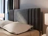 A close-up view of a bed with a grey upholstered headboard and white pillows. Produktbild-Vorschau