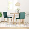 Two dark green fabric dining chairs are placed around a round wooden dining table in a bright, naturally lit room with a window and blinds. Anteprima dell’immagine prodotto