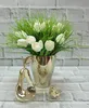 A gold ceramic vase with white tulips and green grass, placed on a table with a gold pear and bird figurine in front of a brick wall. Anteprima dell’immagine prodotto