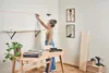 A woman is using a laser level to mark a line on the wall above a shelf. Podgląd zdjęcia produktu
