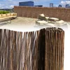 A rooftop patio with furniture and a bamboo fence, with a rolled-up bamboo fence in the foreground. Produktbild-Vorschau