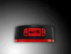 A close-up studio shot of a black and red alarm clock with a digital display. Produktbild-Vorschau