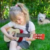 A young girl playing a guitar in a grassy outdoor setting with a dog in the background. Náhled obrázku produktu