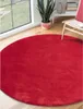 A red circular rug is shown in a room with a large window, a plant, and a chair. Produktbild-Vorschau