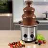 A chocolate fountain with chocolate flowing down, surrounded by fruits and chocolate-covered skewers, in a kitchen setting. Podgląd zdjęcia produktu