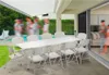 People gathered around a long white table on a patio with a pool in the background. Produktbild-Vorschau
