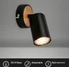 A black adjustable wall light with a wood accent, mounted on a gray wall. Produktbild-Vorschau
