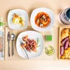 A top-down view of a table setting with multiple plates of food, cutlery, a drink, and a tray of pastries. Náhled obrázku produktu