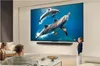 A family is watching a large TV screen displaying dolphins swimming in the ocean. A young girl is pointing at the screen. Voir les images du produit