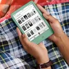 A person is holding a green Kindle e-reader while sitting on a blanket. Náhľad obrázku produktu