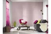 A living room scene with a pink wall, a grey sofa, a pink armchair, a coffee table, and decorative items. Produktbild-Vorschau