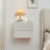 A white marble-effect floating nightstand with two drawers, a lamp, and a cup on top, next to a bed and curtains. Anteprima dell’immagine prodotto