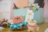 Two plush toys, a bear and a hamster, are displayed on a wooden surface with a light blue bin and office supplies in the background. Produktbild-Vorschau