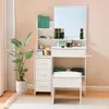 A white vanity table with a mirror, drawers, and a stool, next to a large potted plant. Voir les images du produit