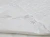 A close-up view of a white quilted mattress protector, showing a care label. Náhled obrázku produktu