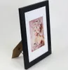 A black picture frame with a white mat and a picture of a woman with a floral headdress. Produktbild-Vorschau