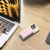 A pink power bank is charging a gold smartphone, which is placed on a wooden desk next to a laptop. Podgląd zdjęcia produktu